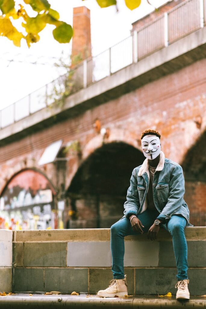 Black man in Anonymous mask sitting on street in daytime